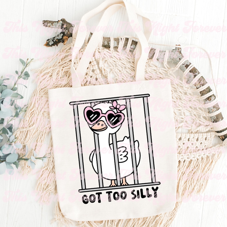 May include: A white tote bag with a cartoon illustration of a goose wearing pink heart-shaped sunglasses and a pink bow. The goose is in a cage and the text "GOT TOO SILLY" is printed below the image.