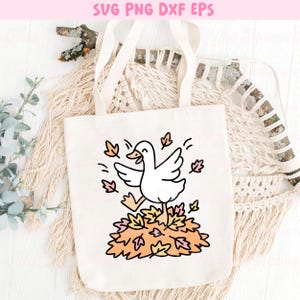 May include: A white canvas tote bag featuring a cartoon goose running through a pile of autumn leaves. The design includes the text "SVG PNG DXF EPS" at the top. The goose is depicted with its wings spread and a happy expression.