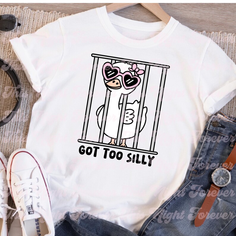 May include: White t-shirt with a cartoon illustration of a goose wearing pink heart-shaped sunglasses and a pink bow. The goose is in a cage with the text "GOT TOO SILLY".