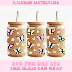 Può includere: Tre involucri per lattine di vetro con coperchi e cannucce in bambù, ciascuno decorato con farfalle, nuvole e cuori colorati. Il testo "RAINBOW BUTTERFLIES" è in alto. Il testo in basso recita "SVG PNG DXF EPS 16OZ GLASS CAN WRAP".