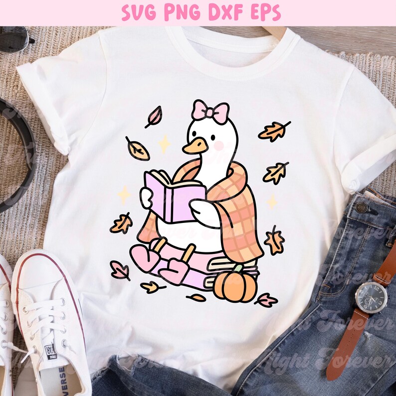 May include: White t-shirt featuring a cartoon goose reading a book, wrapped in a plaid scarf, and surrounded by autumn leaves. The goose wears a pink bow and is sitting on books with a pumpkin. Text at the top reads "SVG PNG DXF EPS".