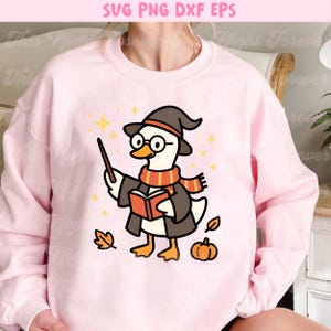 May include: Pink sweatshirt with a cartoon illustration of a wizard goose wearing a hat, glasses, and scarf, holding a wand and book. The design includes fall-themed elements like leaves and a pumpkin, with the text "SVG PNG DXF EPS" at the top.