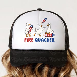May include: A black and white trucker hat with a white front panel featuring a cartoon design of ducks with fireworks. The text "FIRE QUACKER" is displayed in red and blue. The hat has a curved brim and a mesh back.
