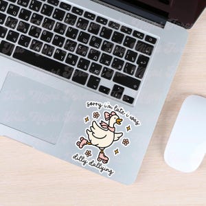 K&ouml;nnte beinhalten: Ein Aufkleber mit einer Cartoon-Ente auf Rollschuhen, mit einer rosa Schleife und einem Schal, mit dem Text "sorry I'm late I was dilly dallying." Der Aufkleber befindet sich auf einem Laptop.