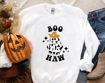 May include: White sweatshirt with a black and white ghost wearing a brown cowboy hat with a yellow star. The text "BOO HAW" is printed in black letters below the ghost.