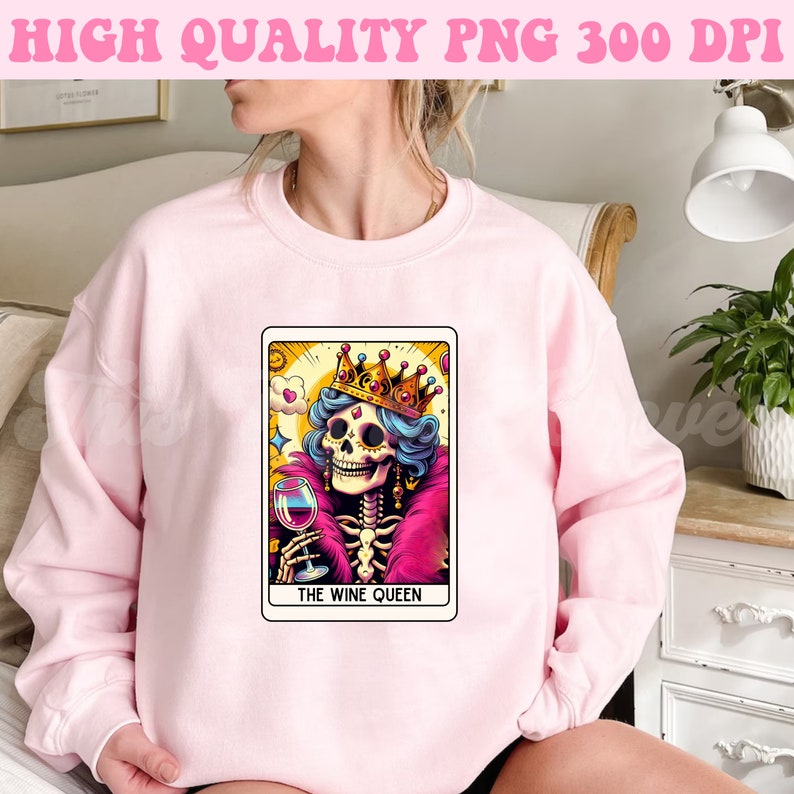 K&ouml;nnte beinhalten: Ein rosa Sweatshirt mit einem Grafikdruck einer Skelettk&ouml;nigin, die eine Krone tr&auml;gt und ein Glas Wein h&auml;lt. Die Grafik ist im Tarotkarten-Stil gehalten und tr&auml;gt den Schriftzug "The Wine Queen".
