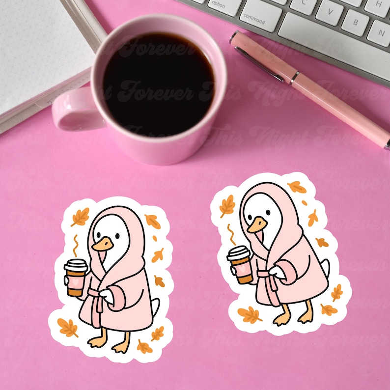 May include: Two stickers featuring a cartoon duck wearing a pink robe and holding a coffee cup. The duck is surrounded by autumn leaves. A pink mug of coffee, a pen, and a keyboard are in the background on a pink surface.