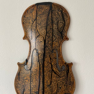 Può includere: Retro di violino in legno con intricati motivi e accenti neri. Il legno ha un tono caldo e naturale, e le linee nere creano un contrasto sorprendente. Il design è dettagliato e artistico, conferendo al pezzo un aspetto unico e artigianale.