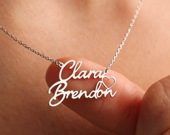May include: Silver necklace with two names, "Clara" and "Brendon", written in cursive script with a small heart symbol between the names.