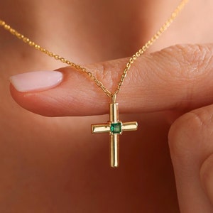 May include: A gold chain necklace with a small gold cross pendant featuring a green gemstone in the center.
