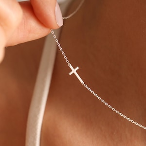 May include: A silver chain necklace with a small, simple cross pendant.