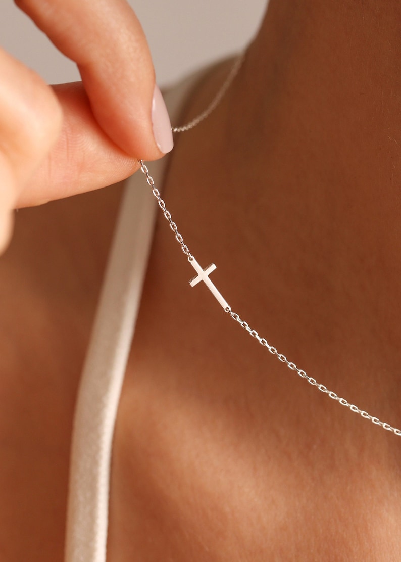 May include: A silver chain necklace with a small, simple cross pendant.