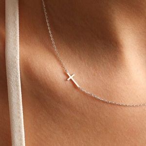 May include: A silver chain necklace with a small silver cross pendant.