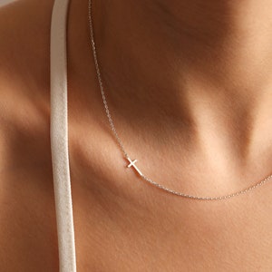 May include: A silver chain necklace with a small silver cross pendant.