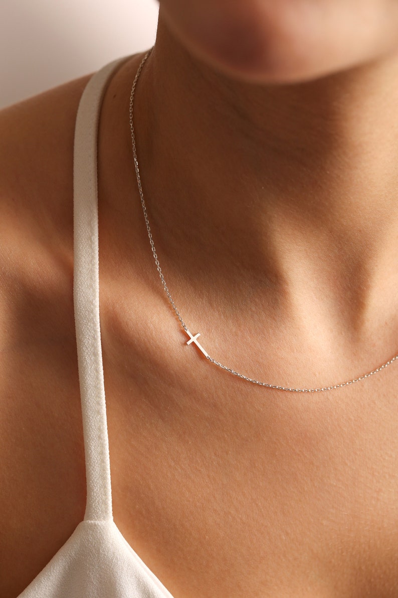 May include: A silver chain necklace with a small silver cross pendant.