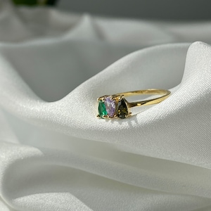 May include: A gold ring with three pear-shaped gemstones. The gemstones are green, purple, and brown.