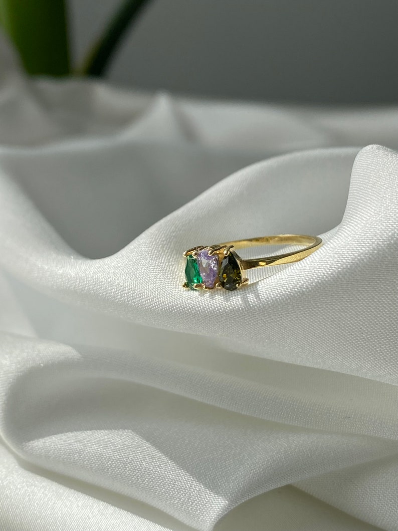 May include: A gold ring with three pear-shaped gemstones. The gemstones are green, purple, and brown.