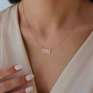 May include: A rose gold necklace with a delicate chain and a pendant featuring the number 1999 in a gothic font.