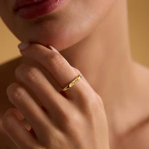 May include: A gold ring engraved with the name "Sophia". The ring has a simple band design, and the text is in a delicate, cursive font. The ring is worn on a finger.