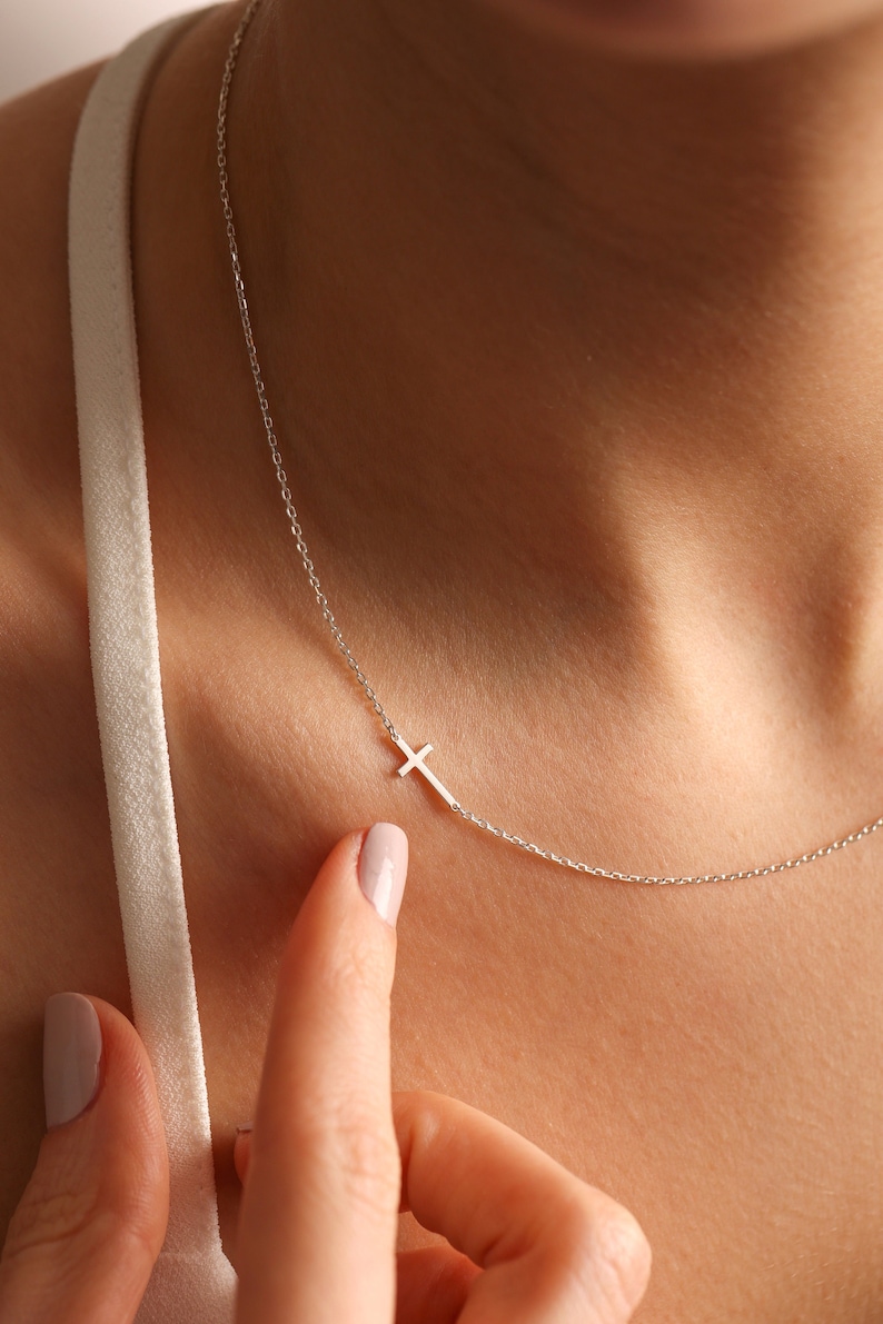 May include: A silver chain necklace with a small, delicate cross pendant.