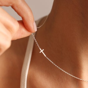 May include: A silver chain necklace with a small, delicate cross pendant.