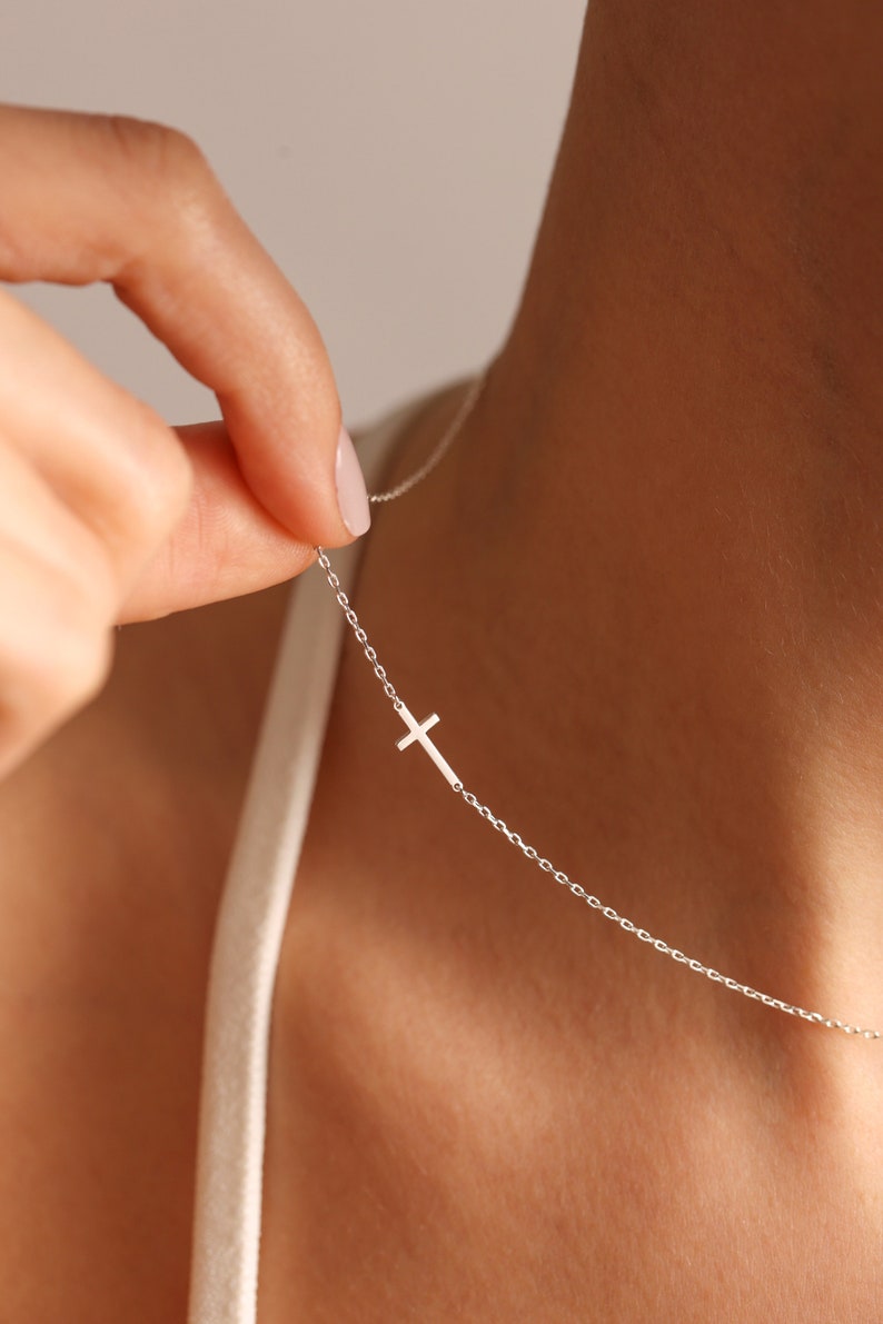 May include: A silver chain necklace with a small, delicate cross pendant.
