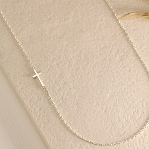 May include: A delicate silver chain necklace with a small, simple cross pendant.