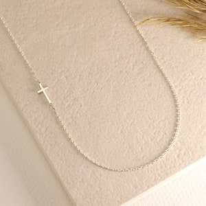 May include: A delicate silver chain necklace with a small, simple cross pendant.
