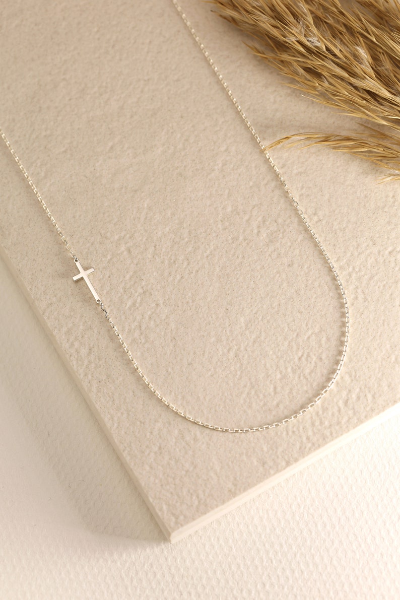 May include: A delicate silver chain necklace with a small, simple cross pendant.