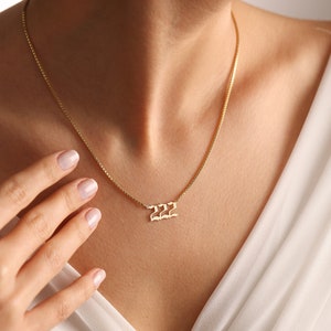 May include: A gold chain necklace with a pendant featuring the number 222 in a stylized font.