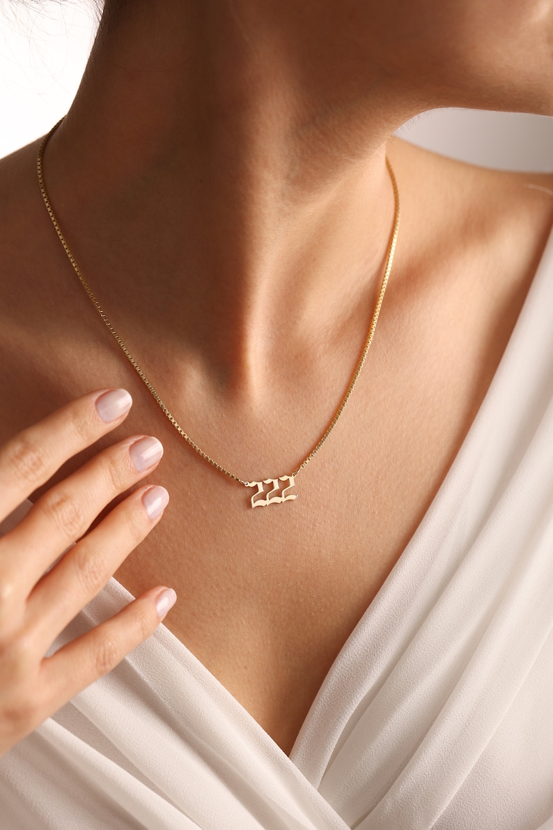 May include: A gold chain necklace with a pendant featuring the number 222 in a stylized font.