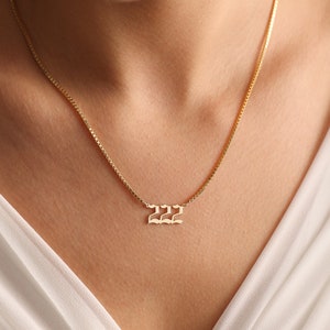 May include: A gold chain necklace with a pendant featuring the number 222 in a gothic font.