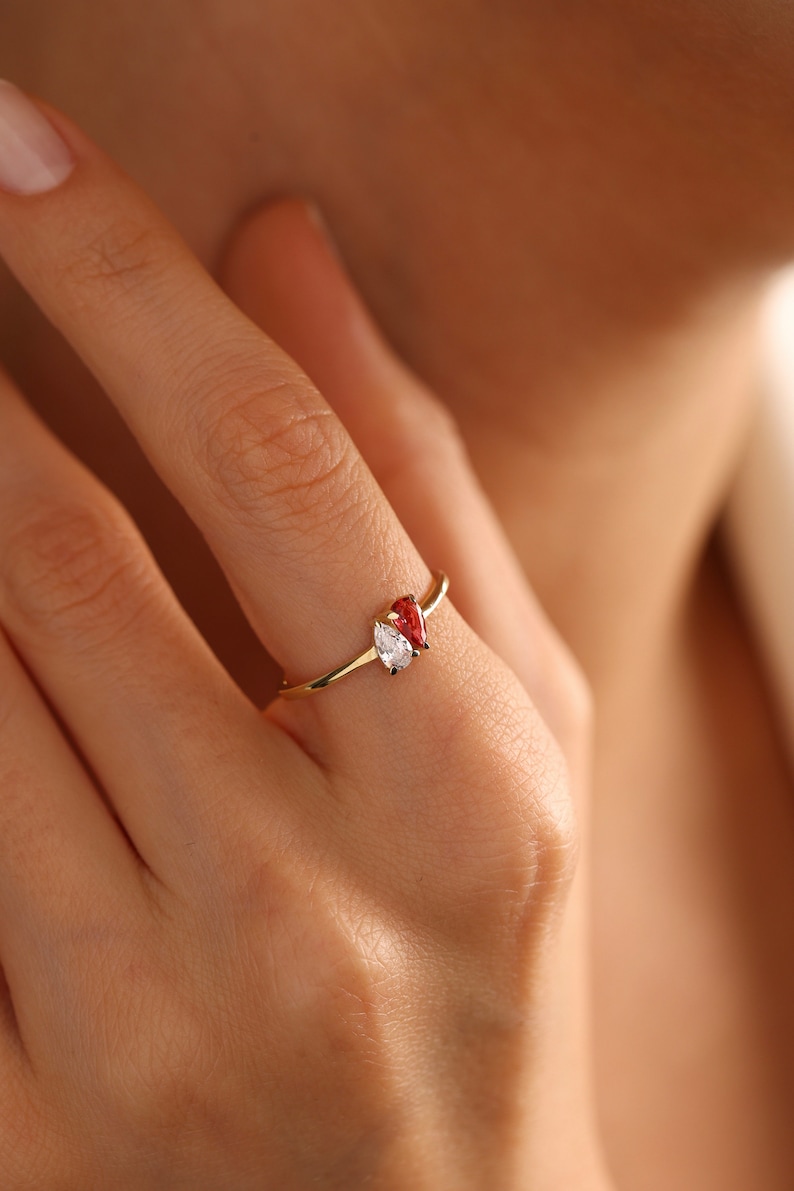 May include: A gold ring with two pear-shaped gemstones. One gemstone is clear and the other is red.
