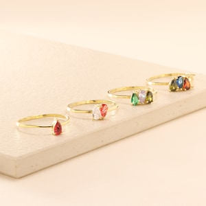 May include: Five gold rings with pear-shaped gemstones. The rings feature red, white, green, blue, and a combination of green and white gemstones.