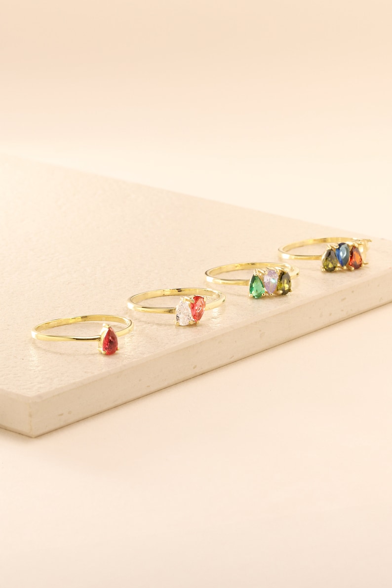 May include: Five gold rings with pear-shaped gemstones. The rings feature red, white, green, blue, and a combination of green and white gemstones.