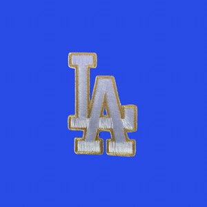 May include: White felt "LA" letters with gold outline. The letters are stitched together and have a slightly raised texture.