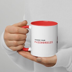 Op de afbeelding: Witte keramische mok met een rode rand en handvat. De mok heeft de tekst "CHANGE YOUR P4$$W0RD123" in zwart gedrukt.