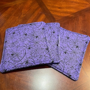 May include: Three purple fabric coasters with a black spiderweb and spider design.