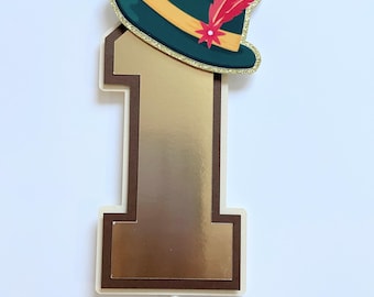 May include: Gold number one cake topper with a green and gold hat with a red feather on top.