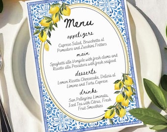 Puede incluir: Un menú de azulejos azules y blancos con un diseño de rama de limón. El menú enumera aperitivos, platos principales, postres y bebidas. El texto dice: "Menú, aperitivos, Ensalada Caprese, Bruschetta al Pomodoro y Buñuelos de calabacín, plato principal, Spaghetti alle Vongole con almejas frescas y Risotto alla Pescatora con mariscos frescos, postres, Tarta de queso de ricotta con limón, Delizia al Limone y Torta Caprese, bebidas, San Pellegrino Limonata, Té helado con cítricos, Smoothies de frutas frescas."