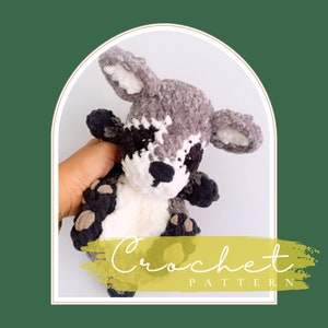 May include: Crocheted raccoon amigurumi toy with gray and white fur, black eyes, and a black nose. The toy is being held by a hand. The image has the text "Crochet Pattern" on a yellow background.