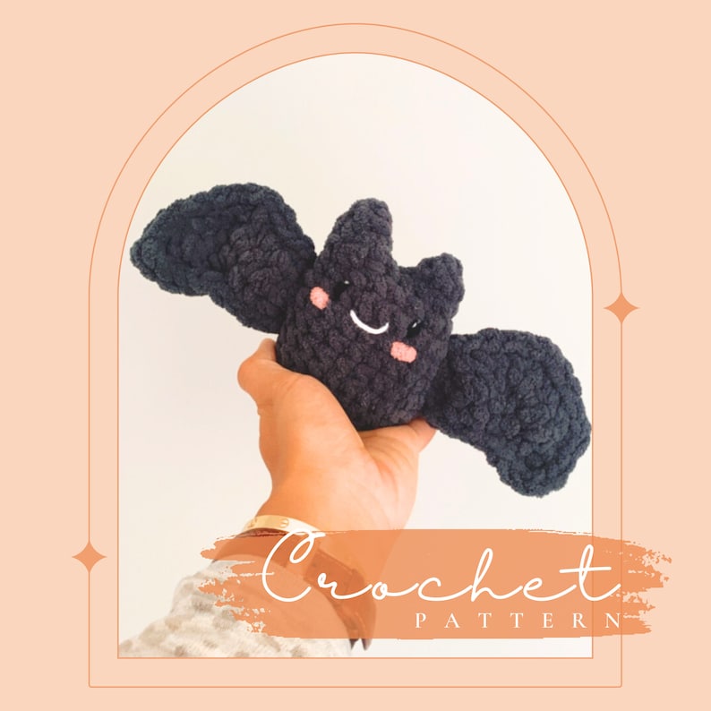 May include: A crocheted black bat with a smiling face and pink cheeks. The bat is being held by a hand with a gold bracelet. The text "Crochet Pattern" is written in white on a peach background.