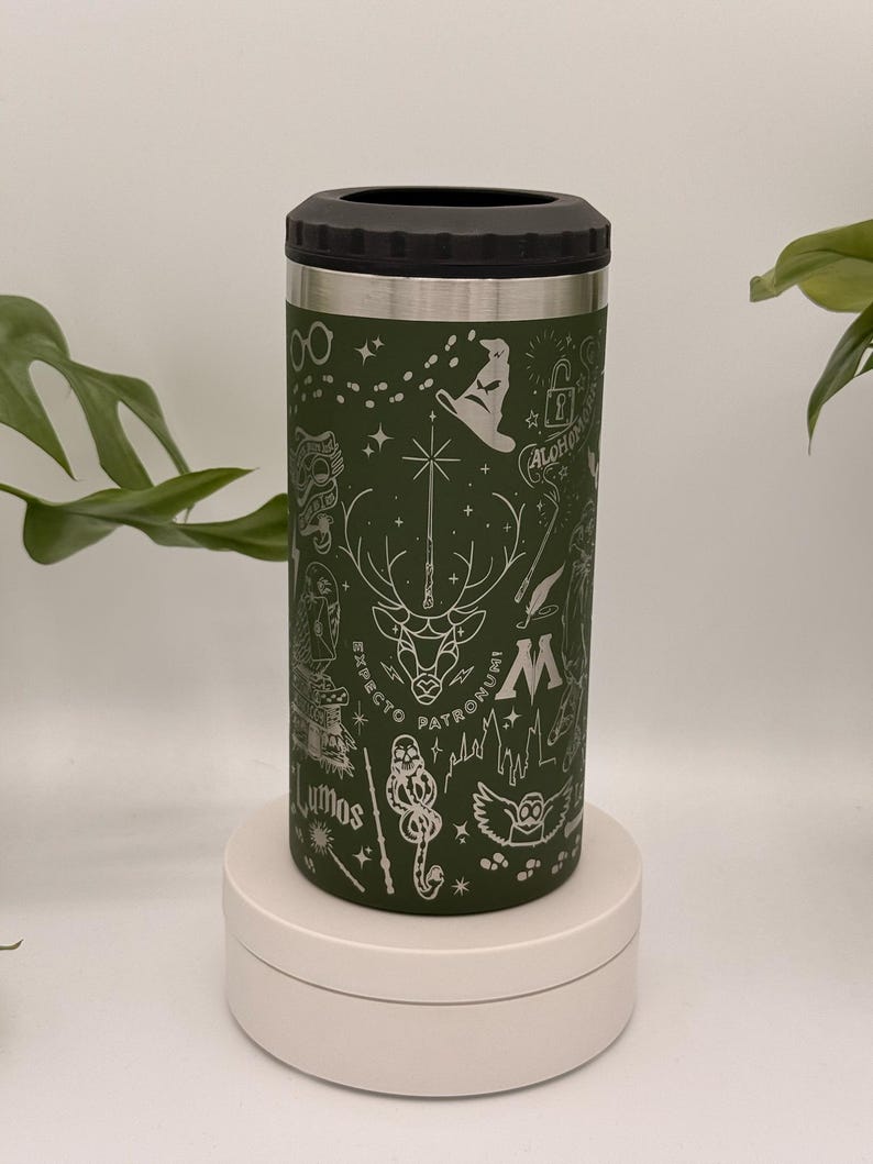 May include: A green insulated drinks holder with a black top, decorated with etched images of a stag, lightning bolt, and other symbols. The words "Expecto Patronum" and "Lumos" are etched on the holder.