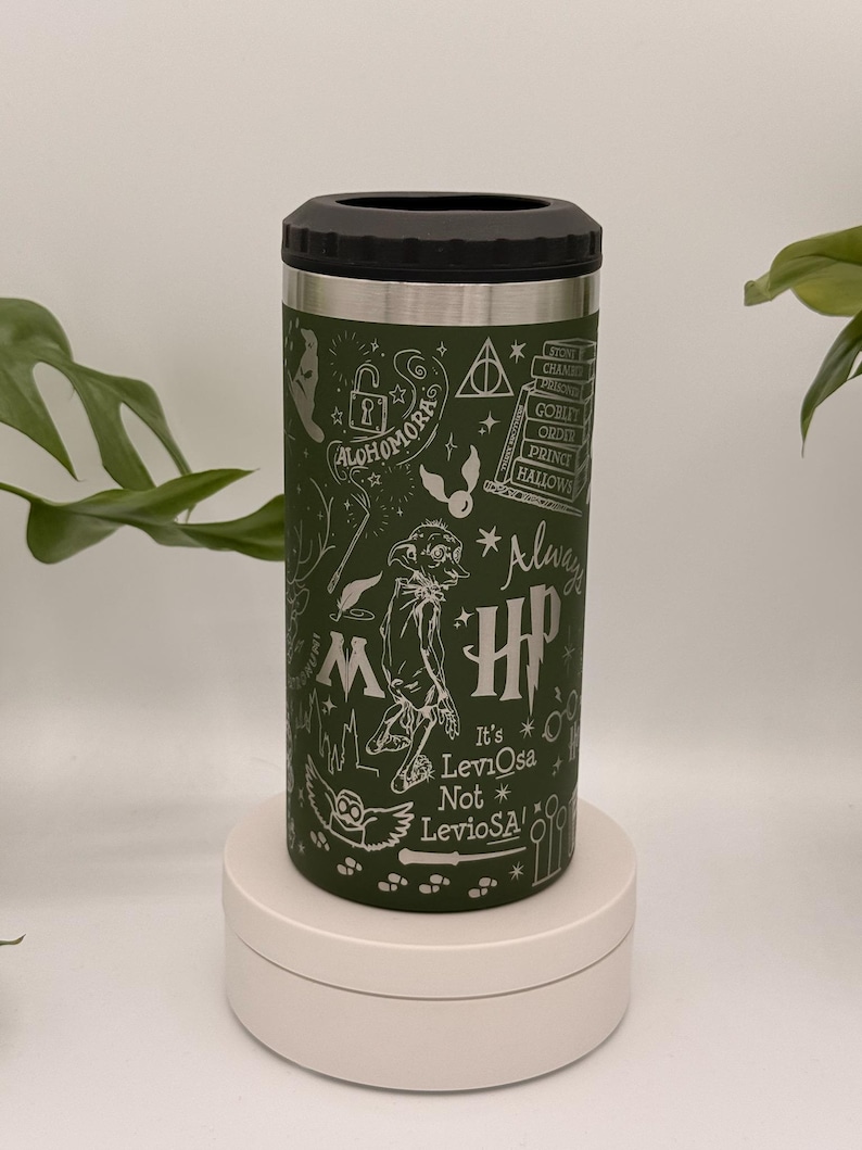 May include: Green insulated drinks tumbler with a black lid and silver trim. The tumbler features white illustrations and text from the Harry Potter series, including the words "Alohomora" and "Always". The text "It's Leviosa Not LevioSA!" is also visible.