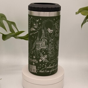 May include: Green insulated drinks holder with a black top and silver rim. The holder features white line art of Hogwarts, a key, and the text "I solemnly swear that I am up to no good." The holder is on a white stand.