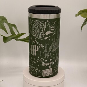 May include: Green insulated drinks holder with a black lid, decorated with white Harry Potter-themed illustrations. The design includes Hogwarts castle, books, and the text "Always" and "Hogwarts". The holder is cylindrical and sits on a white platform.