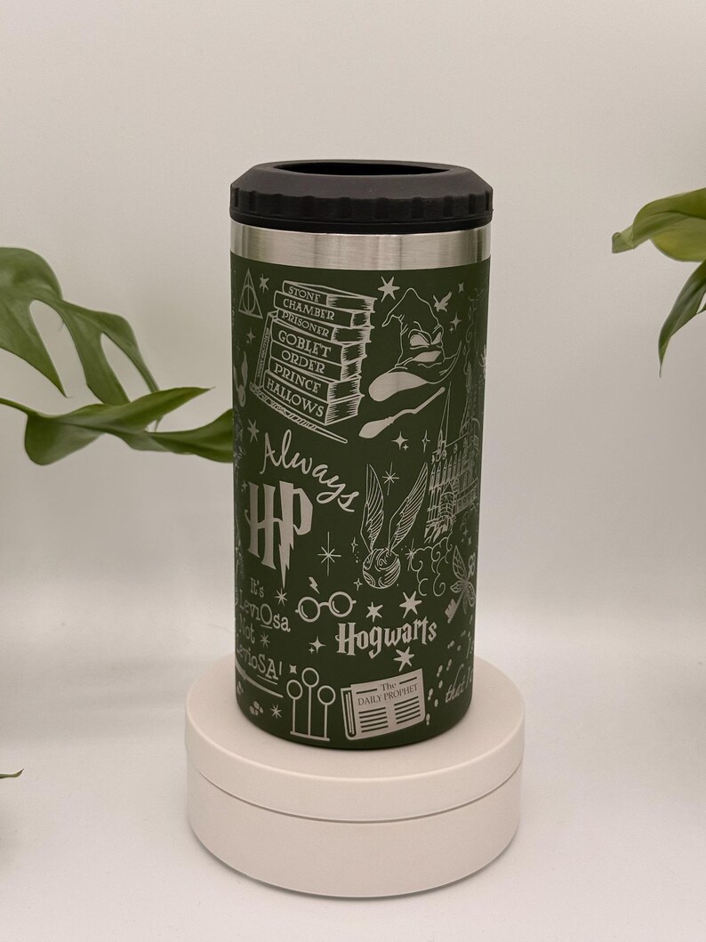May include: Green insulated drinks holder with a black lid, decorated with white Harry Potter-themed illustrations. The design includes Hogwarts castle, books, and the text "Always" and "Hogwarts". The holder is cylindrical and sits on a white platform.