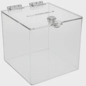 May include: A transparent, square acrylic donation box with a slot on the top and a hinged lid. The box features a locking mechanism, suitable for collecting money or ballots. The box is empty and is set against a white backdrop.