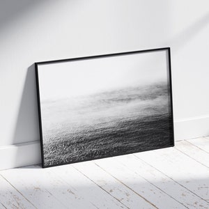 May include: A black and white photograph of a foggy ocean scene framed in a black frame.