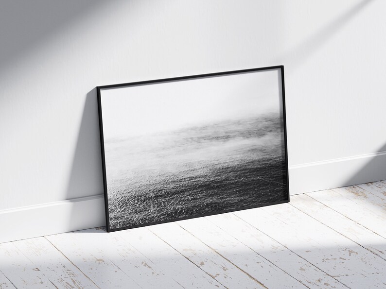 May include: A black and white photograph of a foggy ocean scene framed in a black frame.
